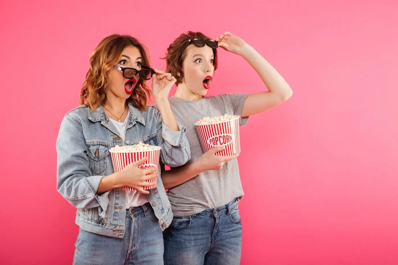 Shocked female friends eat popcorn as they watch a film.