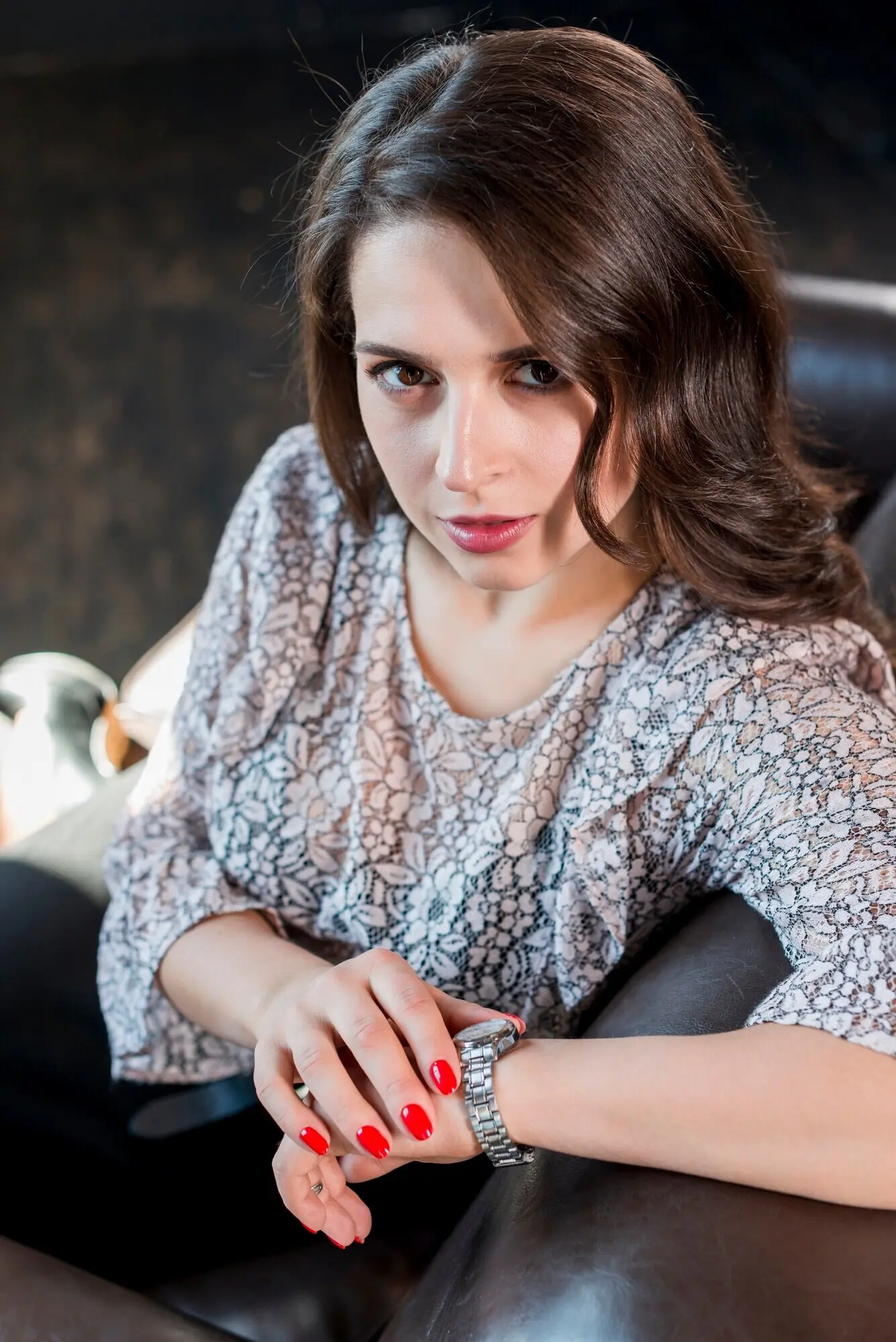 An overhead shot of a young woman holding a wristwatch in her hand, looking at the camera.